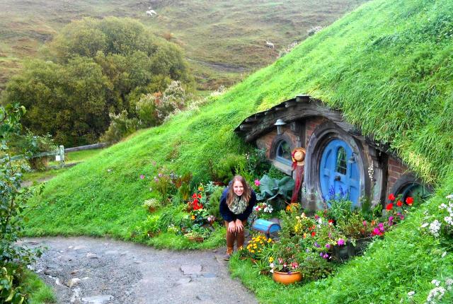 a student poses next to a Hobbit hole in Hobbiton movie set from the Lord of the Rings