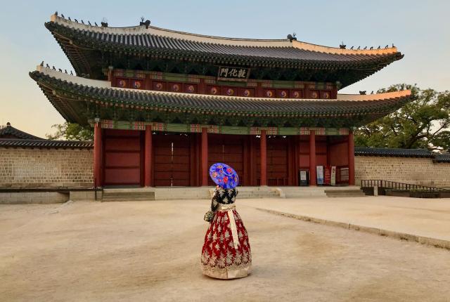 a student poses for a photo at Changdeokgung Palace in Seoul in a traditional Korean hanbok dress and umbrella