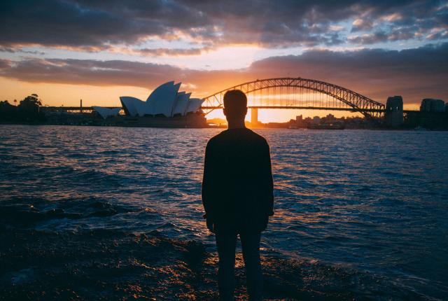 an artistic shot of a student looking at Sydney Opera House and Bridge at sunset