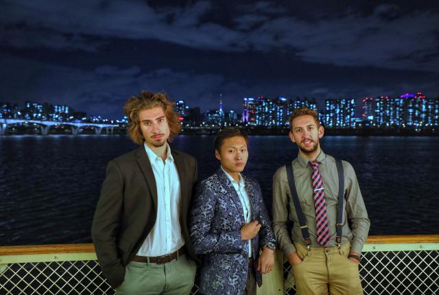 three students pose for a photo in front of the Seoul skyline at night