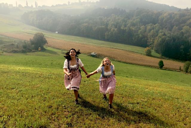 students running up a hill in dirndl dresses on the boarder of Austria