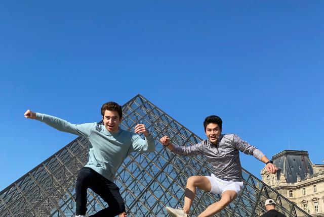 two students jump into a pose for a photo in front of the Louvre