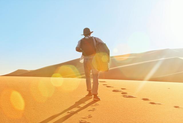 a student walking in the Sahara Desert with a hat and backpack on