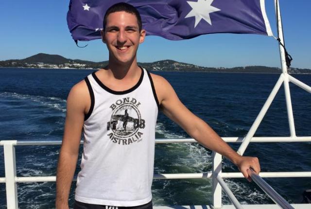 a student poses for a photo while on a boat with the Australian flag blowing behind them