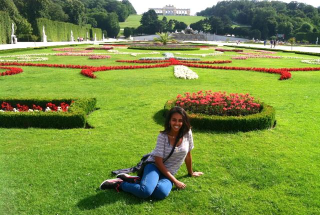 a student posing for a photo while sitting on the ground at Schönbrunn Palace in Vienna on a sunny day among flowers