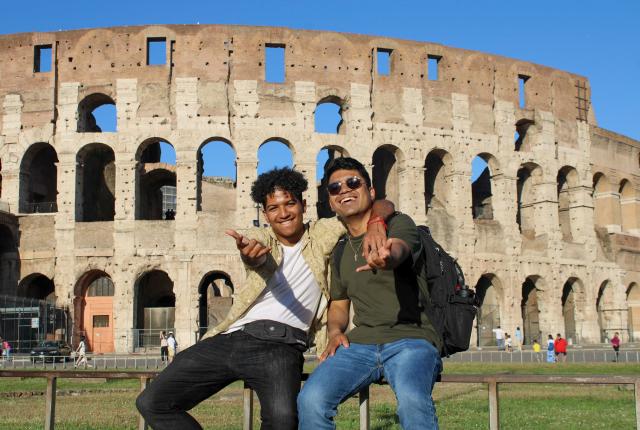 two male students pose for a fun photo in front of the Roman Colosseum in Italy
