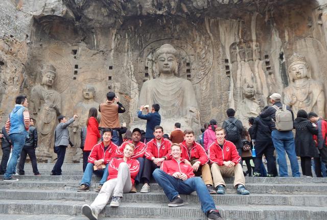 engineering students sitting on the steps in front of a stone carving of buddha