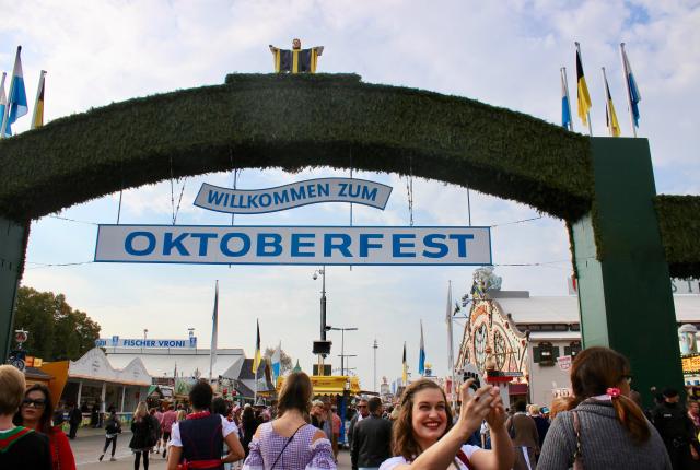 a girl in dirndl taking a selfie in front of the Oktoberfest entrance