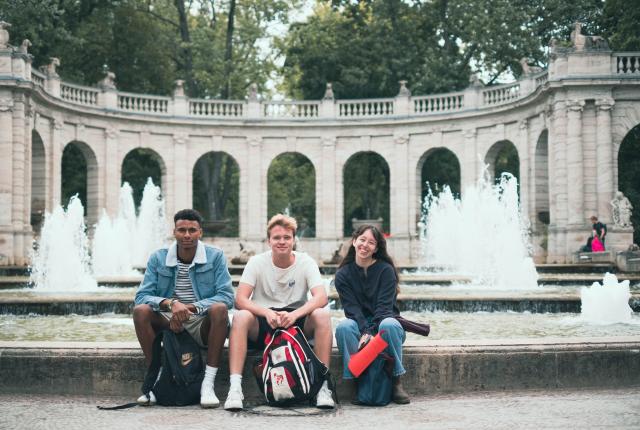 Three students sit on the edge of Märchenbrunnen foundation in Berlin.