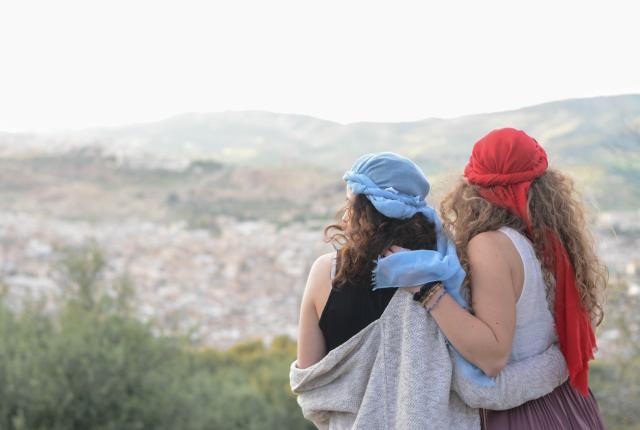 Two students in Morocco wearing red and blue headscarves look out over the city.