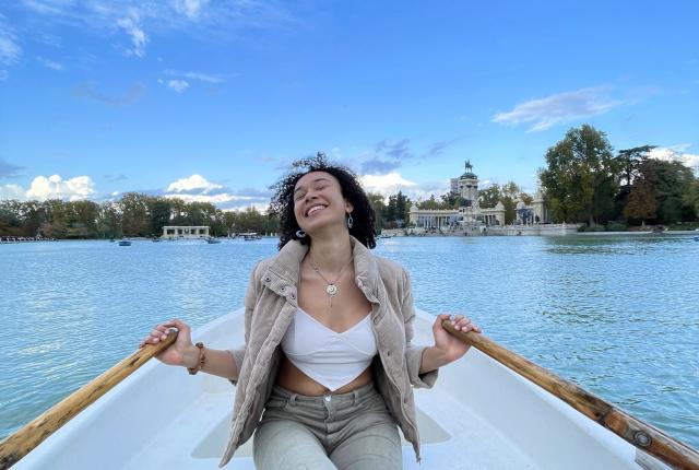 A student is smiling in a white boat in Madrid, Spain as she paddles with two oars.
