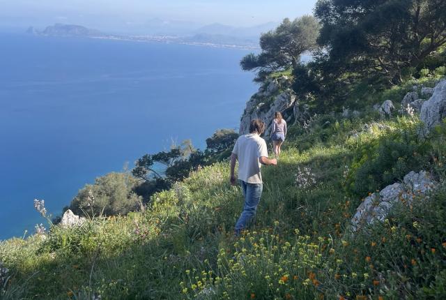 Two students hiking on a grassy mountain near the Mediterranean coast in Italy.