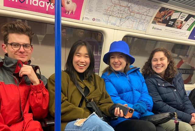 four students sitting on seats in the london tube passing a station