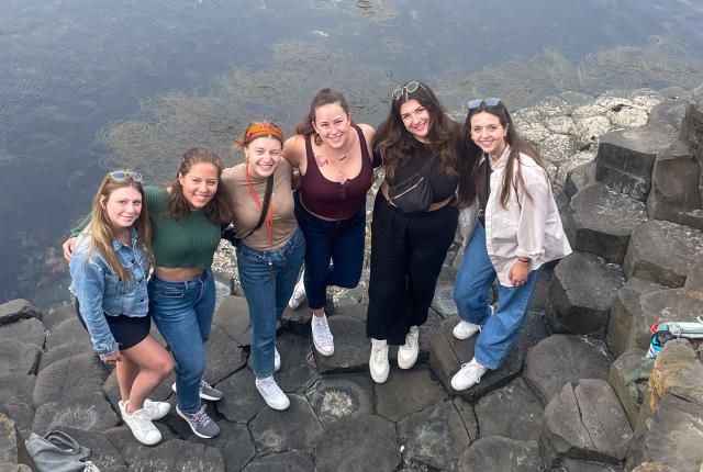students standing on hexagonal rock formations at the giant's causeway in front of the ocean