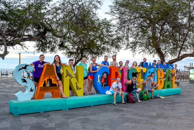 a cohort of students pose for a photo with the San Cristobal Galápagos sign