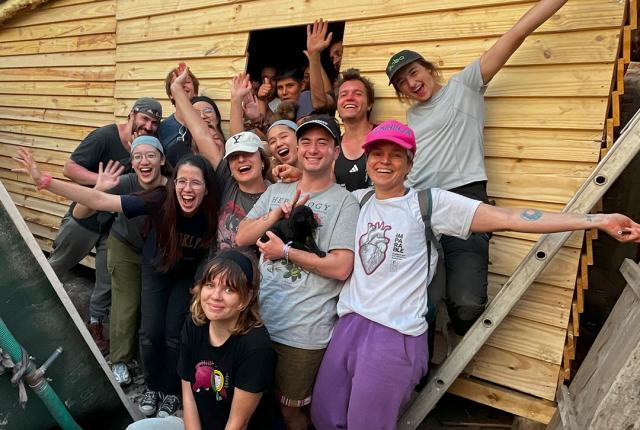 a group of students pose for a photo with a transitional home they built for a family in need