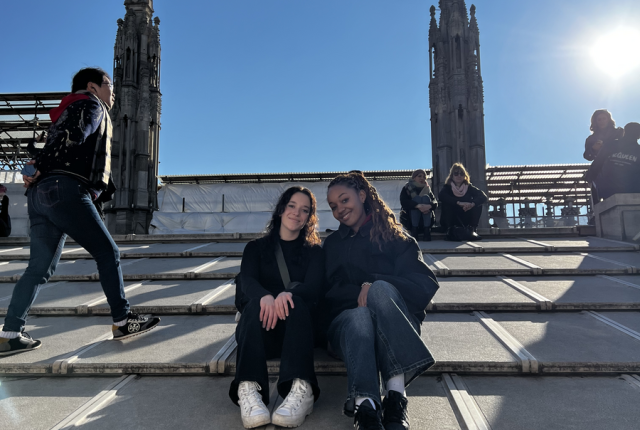 Two friends sitting on the roof of the Milan Duomo with other people in the background and sun shining down