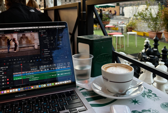 A cup of coffee and a laptop with video editing software at a cafe in front of the Colosseum.