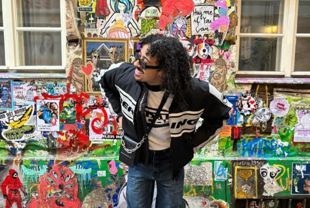 Myles smiling in front of a wall covered in stickers.