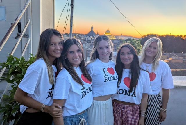 Five students smile in front of a sunset wearing I heart Roma t-shirts.