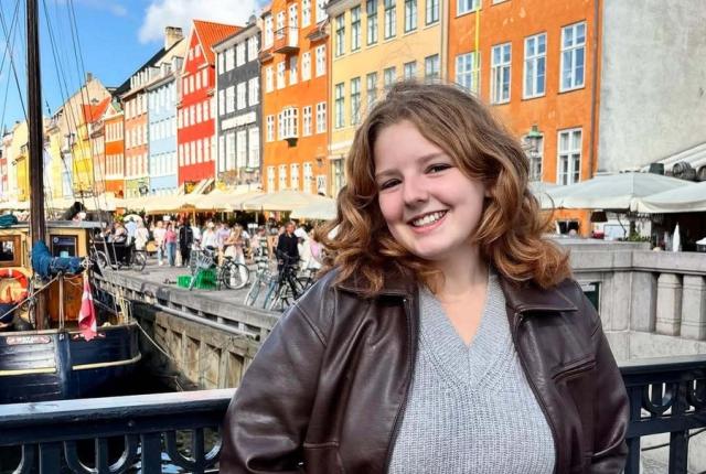 Female student smiling with a backdrop of colorful buildings and a river in Amsterdam 