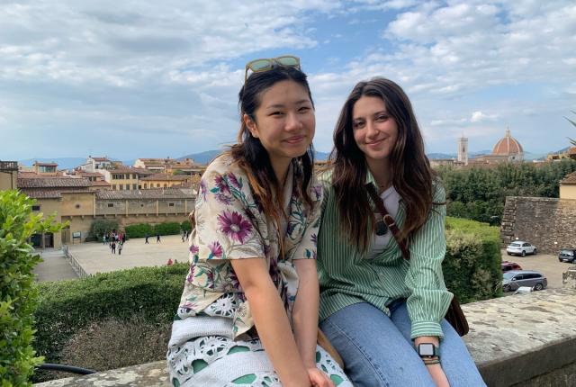 Two girls sitting on a ledge in Florence italy with the city behind them and clouds