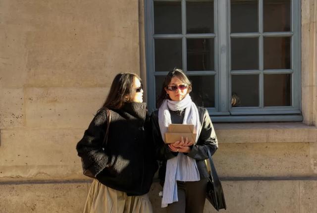 Two students holding books against a wall 