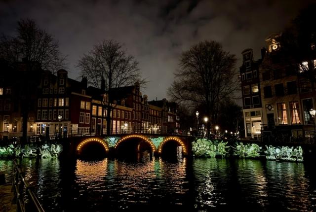 Amsterdam Canal at night with a glowing bridge, reflections on the water, and historic buildings lining the waterfront
