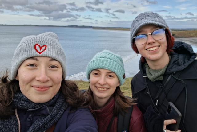Three students standing on a coastal overlook in Ireland, with the shoreline and open water stretching into the distance behind them.