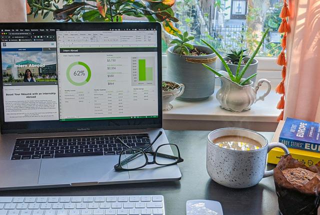 A laptop with the IES Abroad internship webpage on it, in front of a window with plants and near a cup of coffee