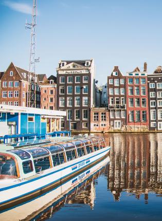 boats sit in Amsterdam Centraal Canal in front of traditional Amsterdam architecture
