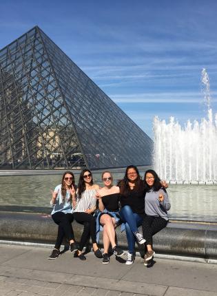 a group of students flash peace signs in front of the Louvre and its fountains