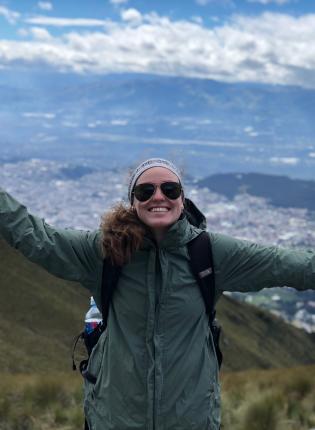 a student poses for a photo from atop the mountains in Quito with a backdrop of the city
