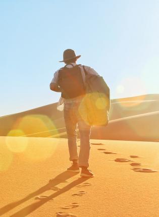a student walking in the Sahara Desert with a hat and backpack on