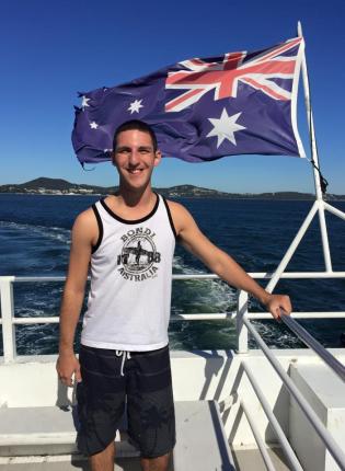 a student poses for a photo while on a boat with the Australian flag blowing behind them