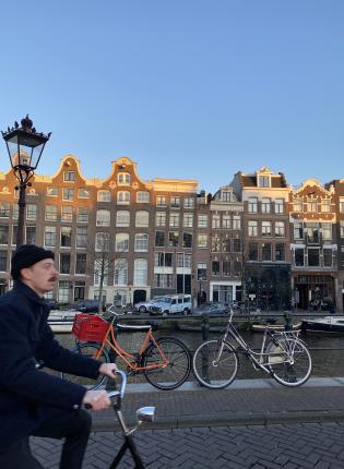 a man riding by on a bike in front of buildings in Amsterdam