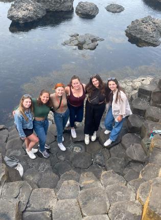 students standing on hexagonal rock formations at the giant's causeway in front of the ocean