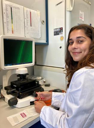 student in white coat sitting at desk in front of microscope and computer