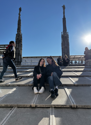 Two friends sitting on the roof of the Milan Duomo with other people in the background and sun shining down