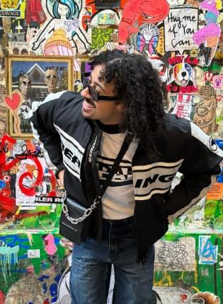 Myles smiling in front of a wall covered in stickers.