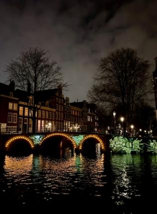 Amsterdam Canal at night with a glowing bridge, reflections on the water, and historic buildings lining the waterfront