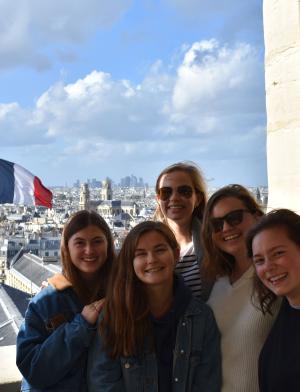 a group of students pose for a photo in front of a French flag and Paris backdrop, including the Eiffel Tower
