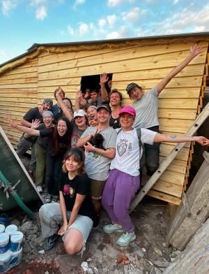 a group of students pose for a photo with a transitional home they built for a family in need