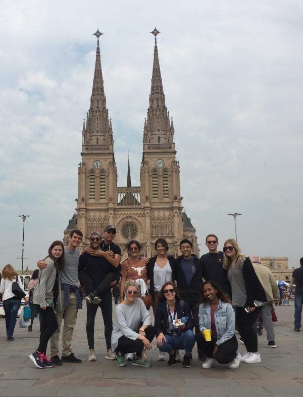 group of students standing in front of a tall, gothic building with two spires on a cloudy day