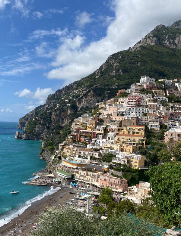 Buildings sit crowded on a hill on the Amalfi coast, with a large rocky outcropping standing tall in the background.