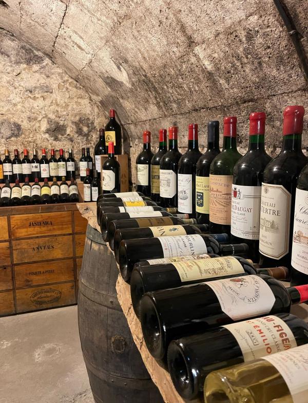 A wine cellar with stone walls, wooden caskets, and rows of bottles of red wine