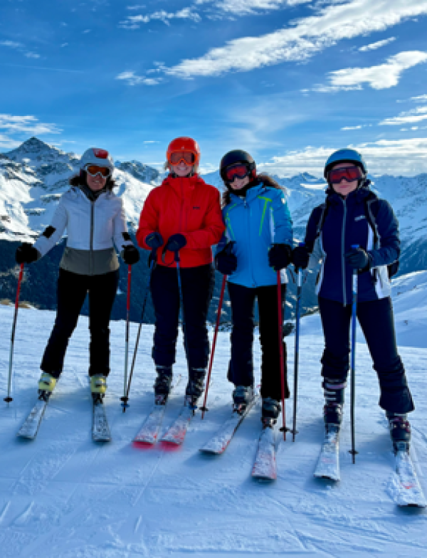 Four students in skiing gear posing atop snow.