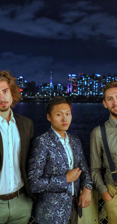 three students pose for a photo in front of the Seoul skyline at night