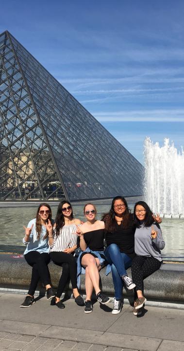 a group of students flash peace signs in front of the Louvre and its fountains