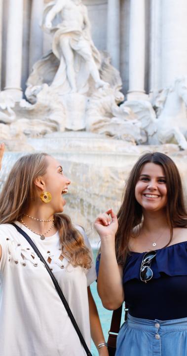 two students posing for a photo in front of Trevi Fountain in Rome as they toss coins in to make a wish